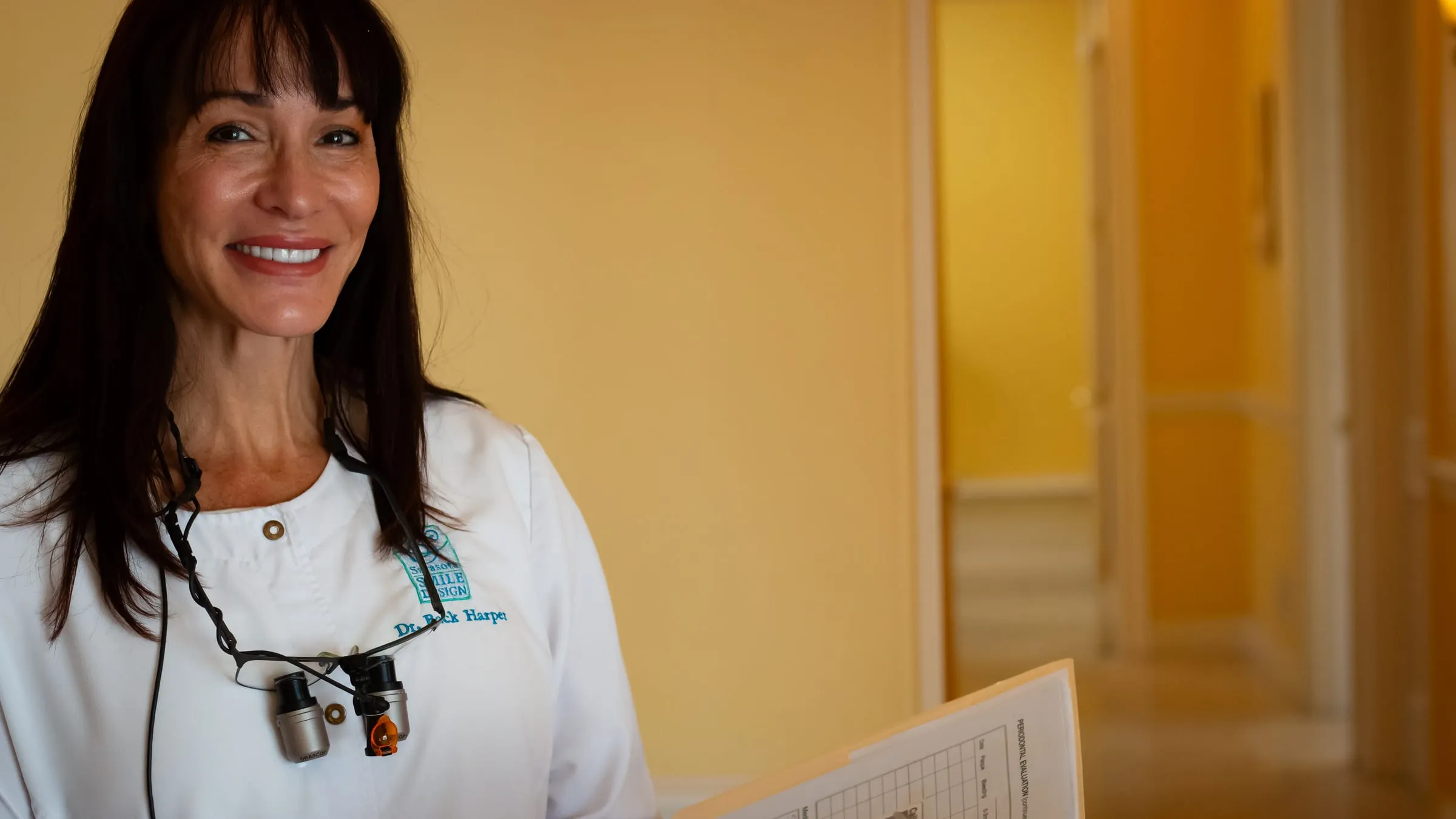Dr. Jenifer Back smiling in the hallway with a patient chart at Sarasota Smile Design in Sarasota, Florida