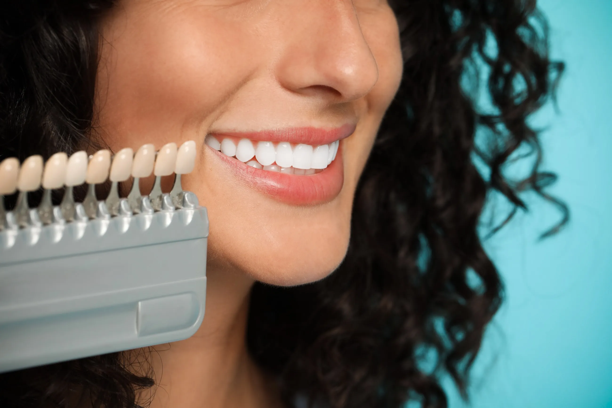 A woman smiling beside a dental shade guide