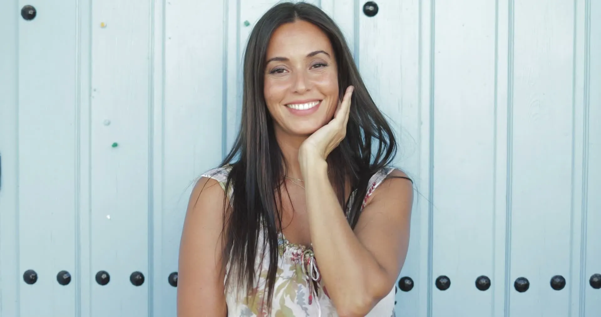A woman smiling against a pale blue wall