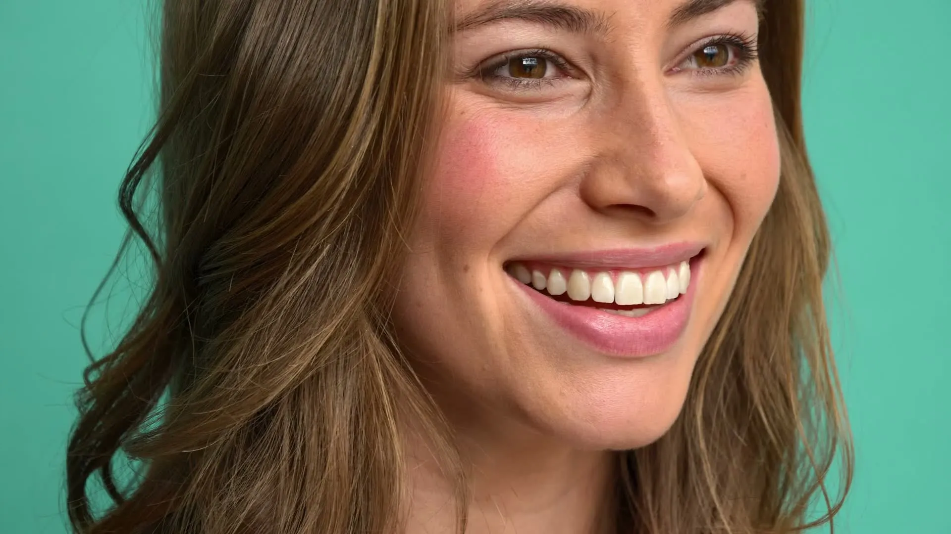A woman smiling against a teal wall