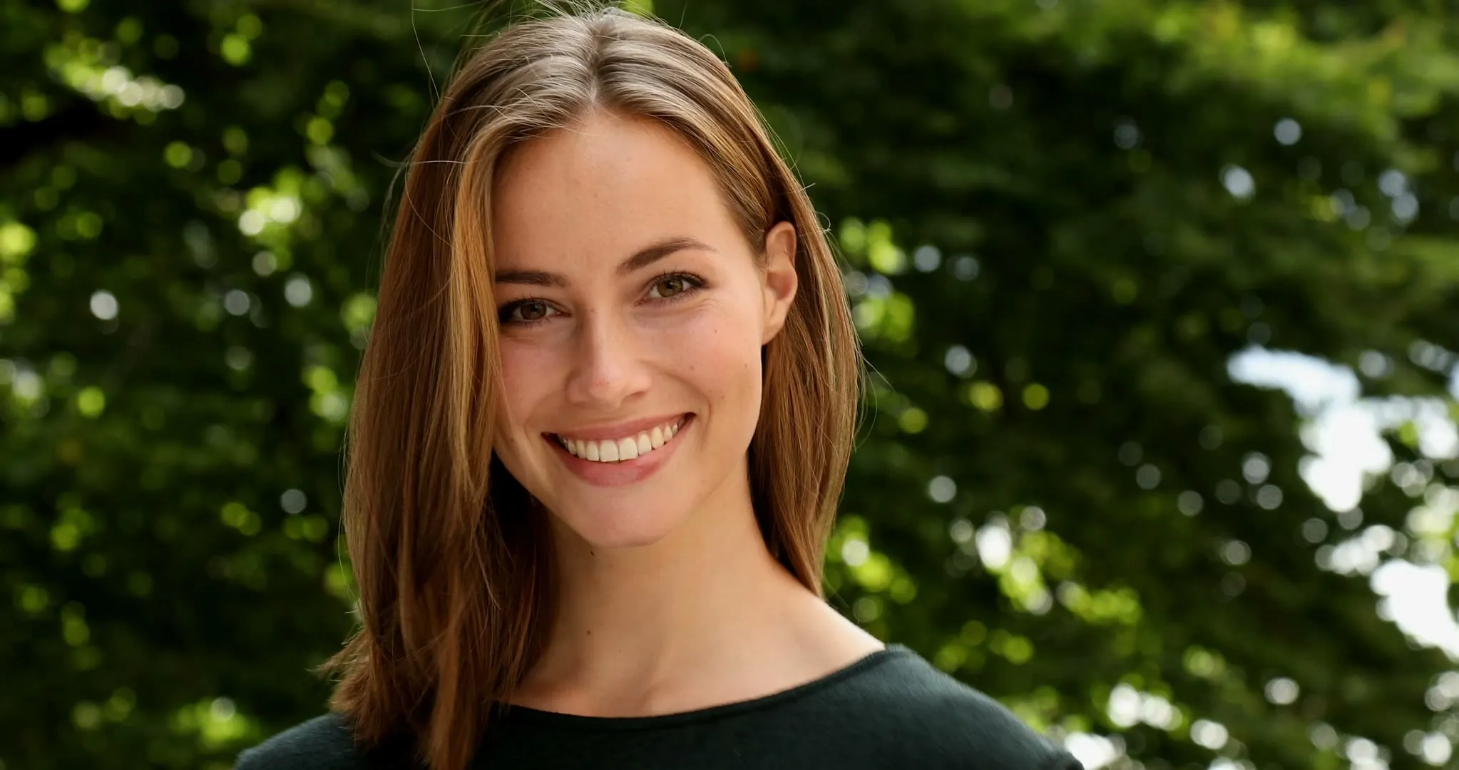 A woman smiling outdoors in sunlight
